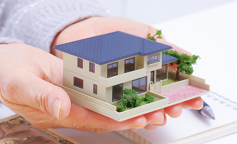 住宅模型を大切に両手で包み込む様子。相続や不動産関連の相談を連想。