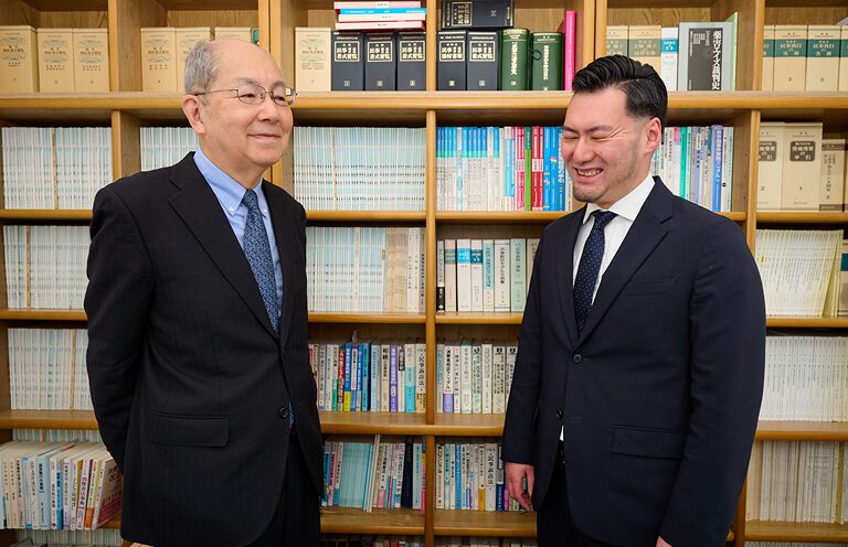 事務所内で談笑するベテランと若手の弁護士。安心感のある雰囲気を伝える。