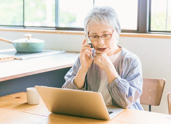 高齢女性が電話とノートパソコンを使って法律相談している様子。