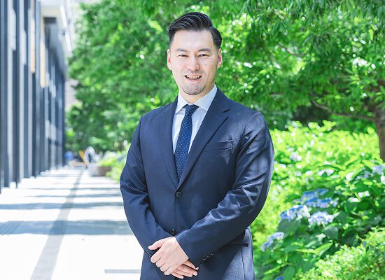 若手弁護士が自然の中で笑顔を見せている写真。爽やかで誠実な印象を演出。