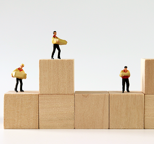 木のブロックの上に立つ作業員のミニチュア。成長や積み重ねを象徴するイメージ。