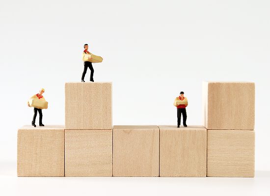 木のブロックの上に立つ作業員のミニチュア。成長や積み重ねを象徴するイメージ。